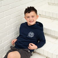 Smiling boy wearing a navy Radiator Hoodie with logo, sitting on white steps.