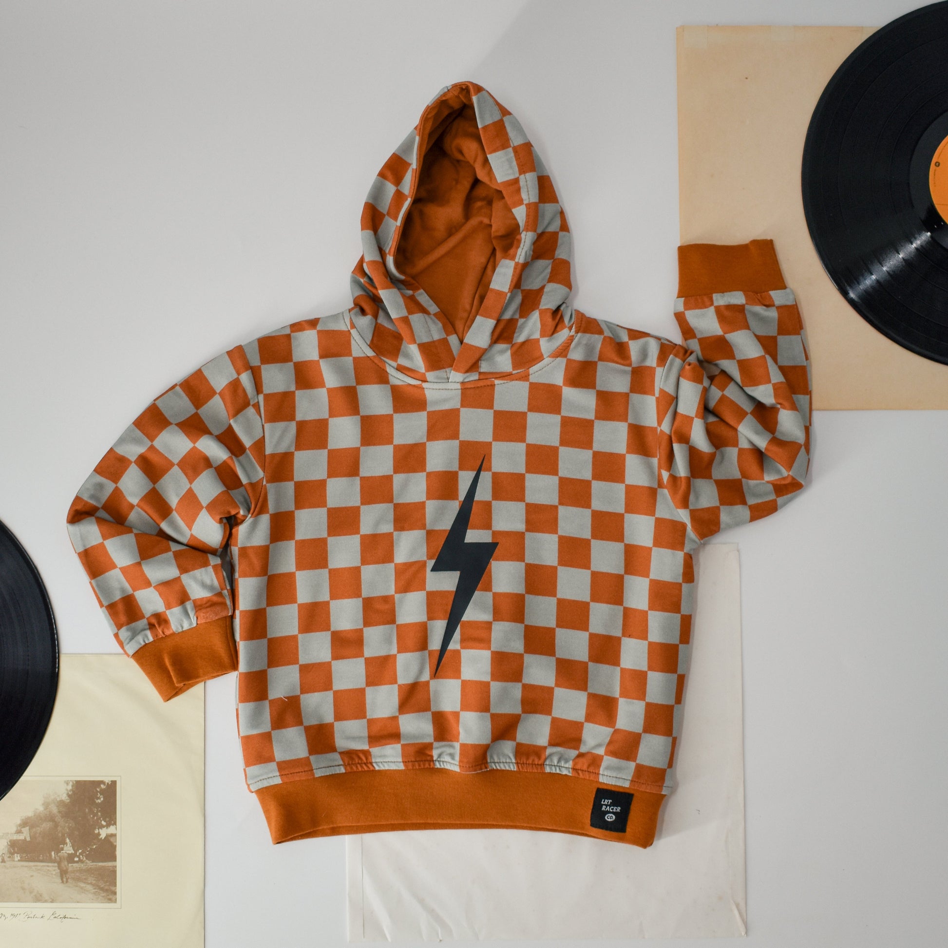 Rust checkered spark hoodie flat lay with vintage record decor.