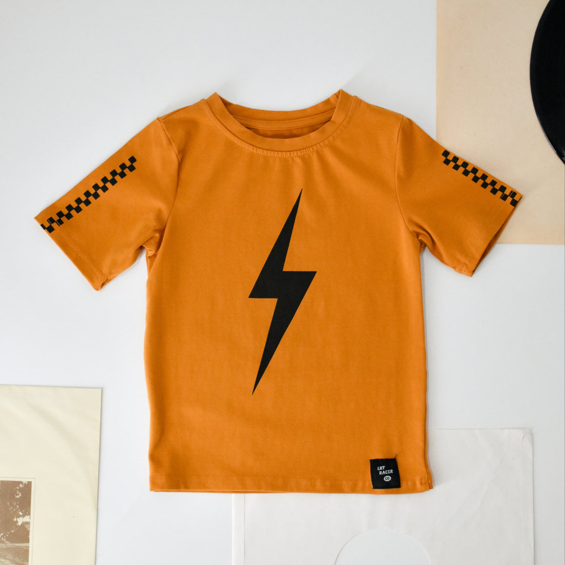 Ocean Cubs Wear: Pumpkin Spark Tee flat lay featuring a lightning bolt and racing stripes.