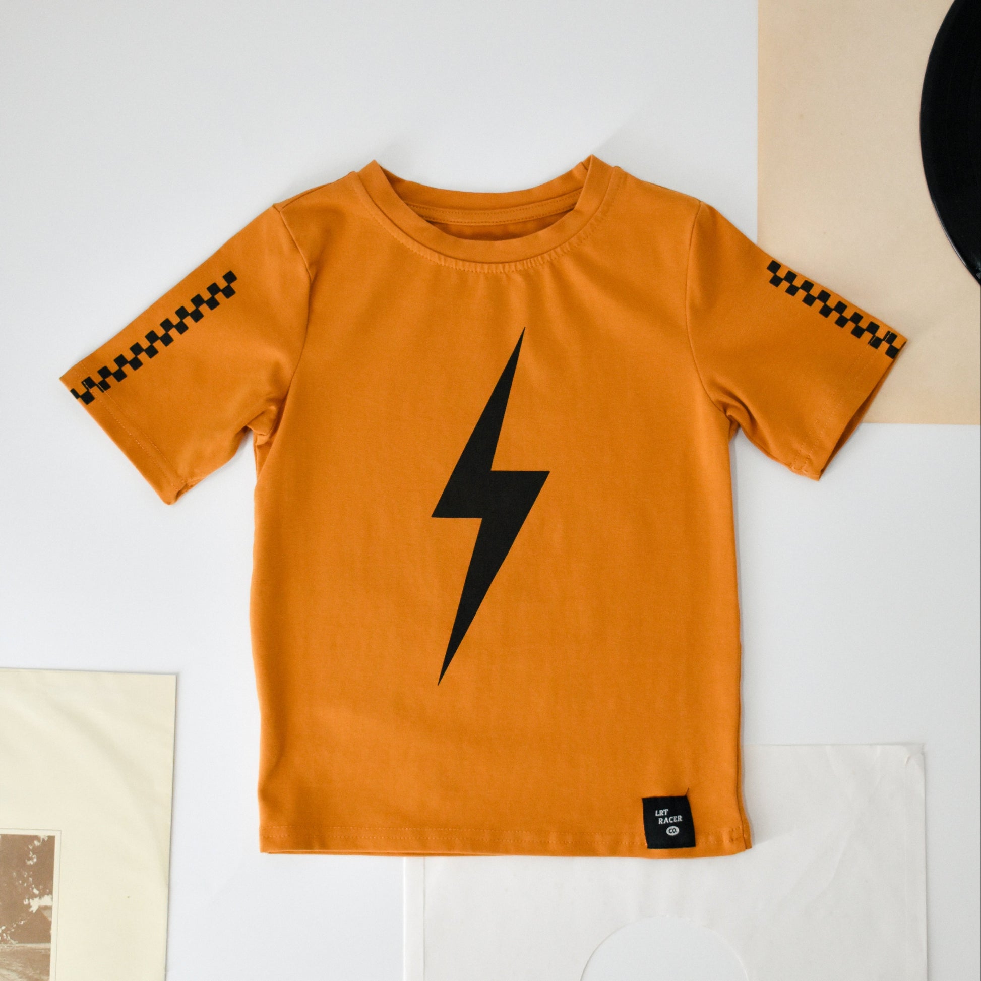 Ocean Cubs Wear: Pumpkin Spark Tee flat lay featuring a lightning bolt and racing stripes.