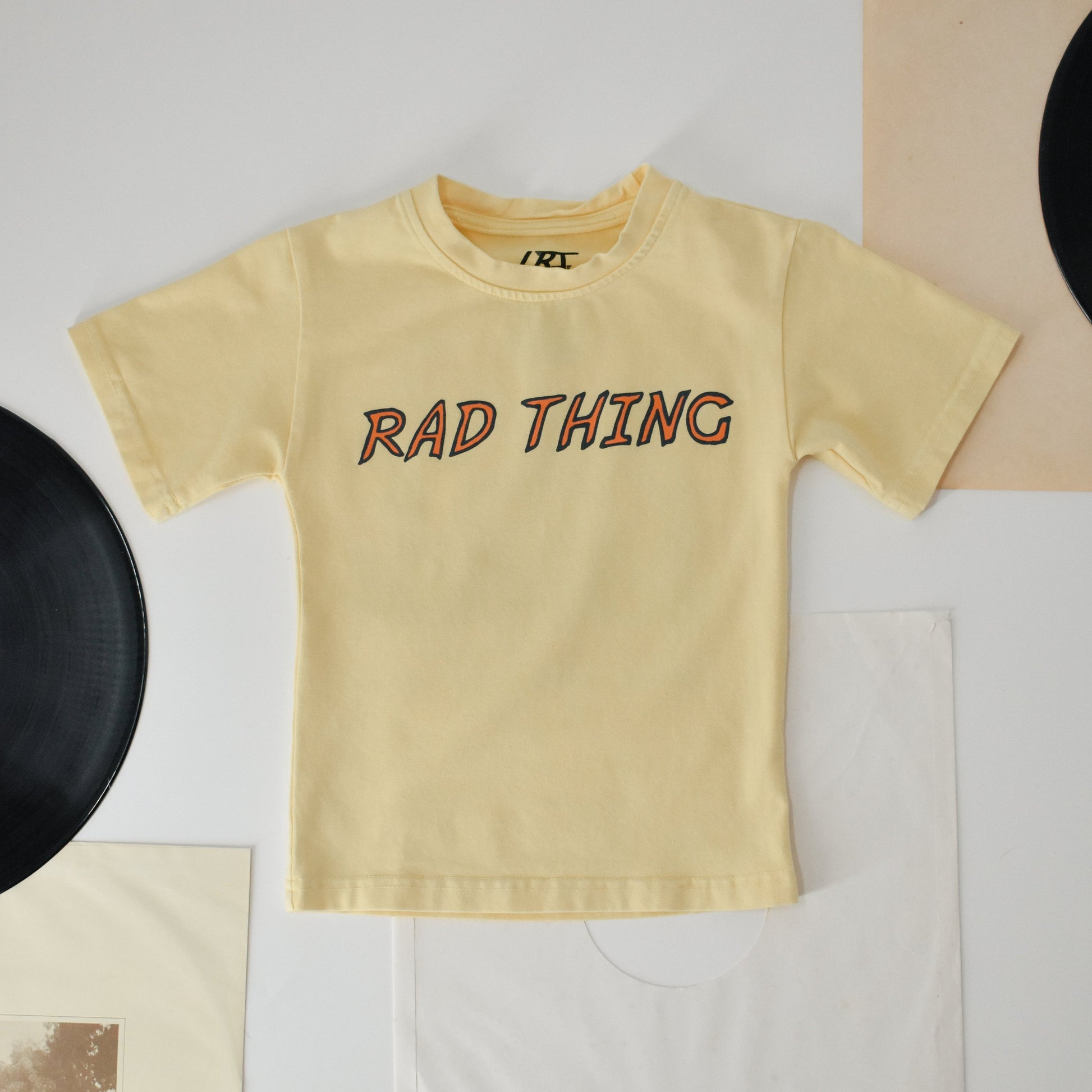 Flat lay of Golden Yellow 'Where the Rad Things Are' tee on white background.