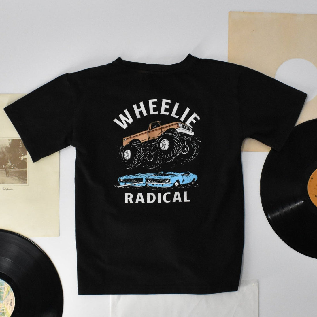 Flat lay of a black Wheelie Radical Tee featuring a monster truck design.