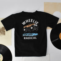 Flat lay of a black Wheelie Radical Tee featuring a monster truck design.