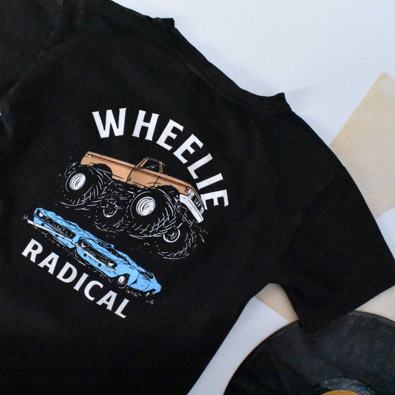 Boy sitting wearing Wheelie Radical Tee with a monster truck and car graphic.
