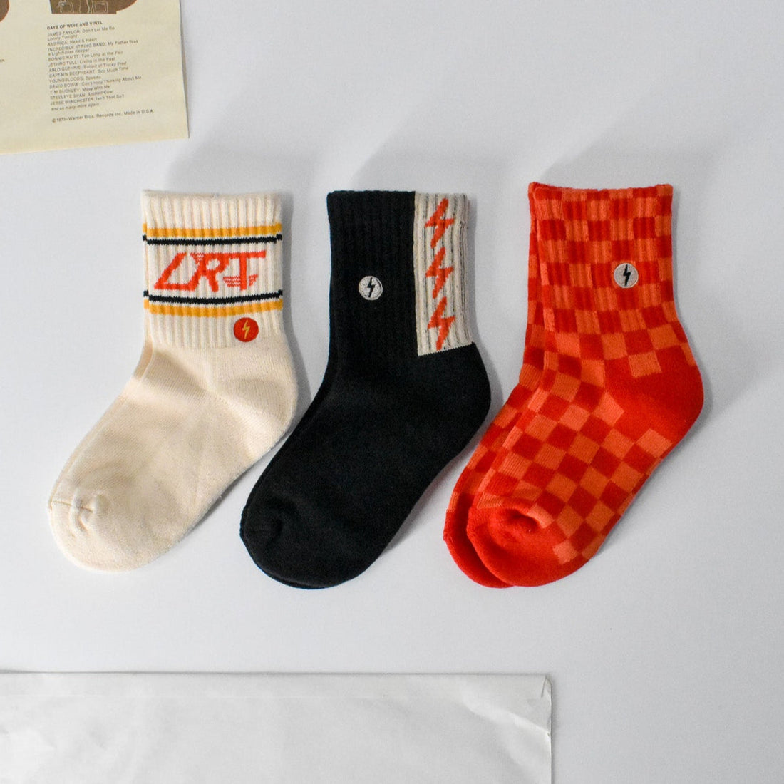 Retrograde 3-pack socks: cream with logo, black with spark, red/orange check.