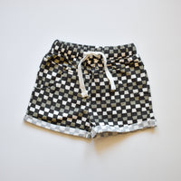 Close-up of black, grey, and white checkered 'Check Ya Later' shorts with drawstring.