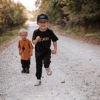 Two boys running; one wears the Juniper Green Explorer Snapback Hat.