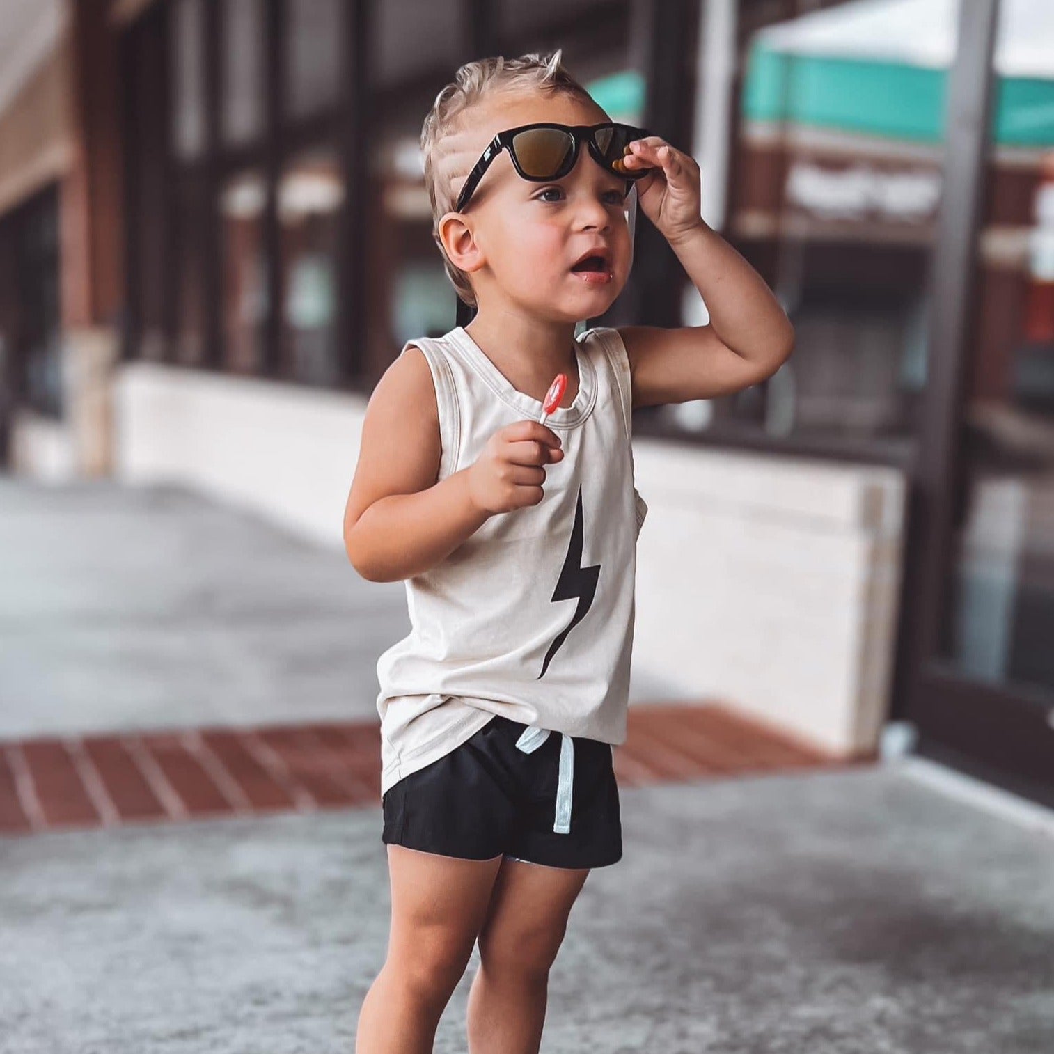 Toddler boy with lollipop wears greige Spark Muscle Tank