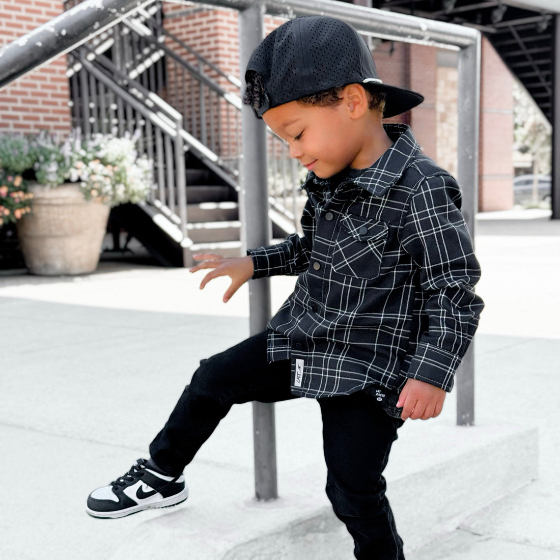 Boy in black and white plaid Kids Flip Side Flannel with black jeans and sneakers.