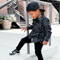 Boy in black and white plaid Kids Flip Side Flannel with black jeans and sneakers.