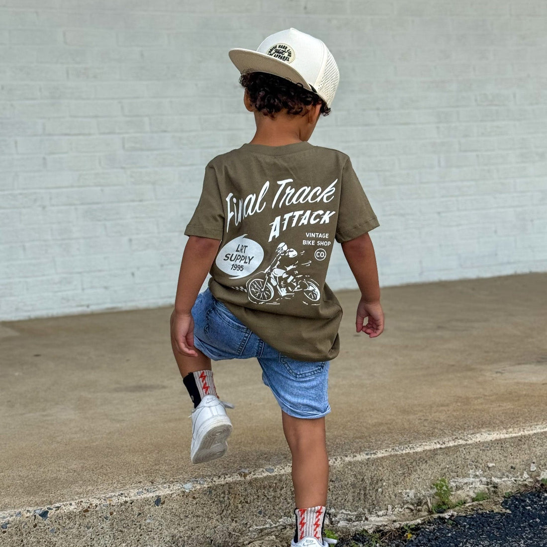 Boy wearing military green Final Track Attack Tee with jean shorts and hat.