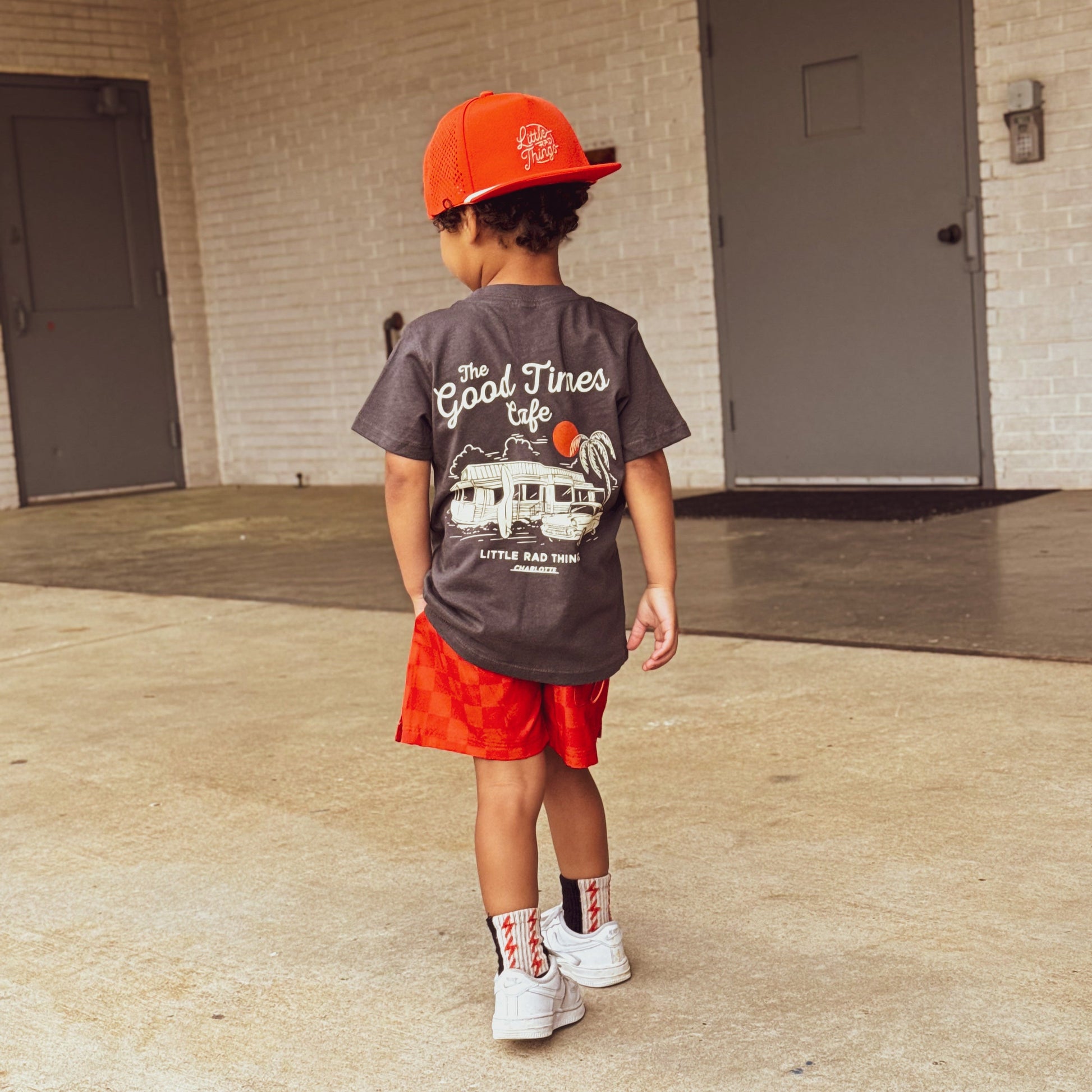 Child in red/orange checkerboard Retro-Wave hybrid board shorts holding a toy.