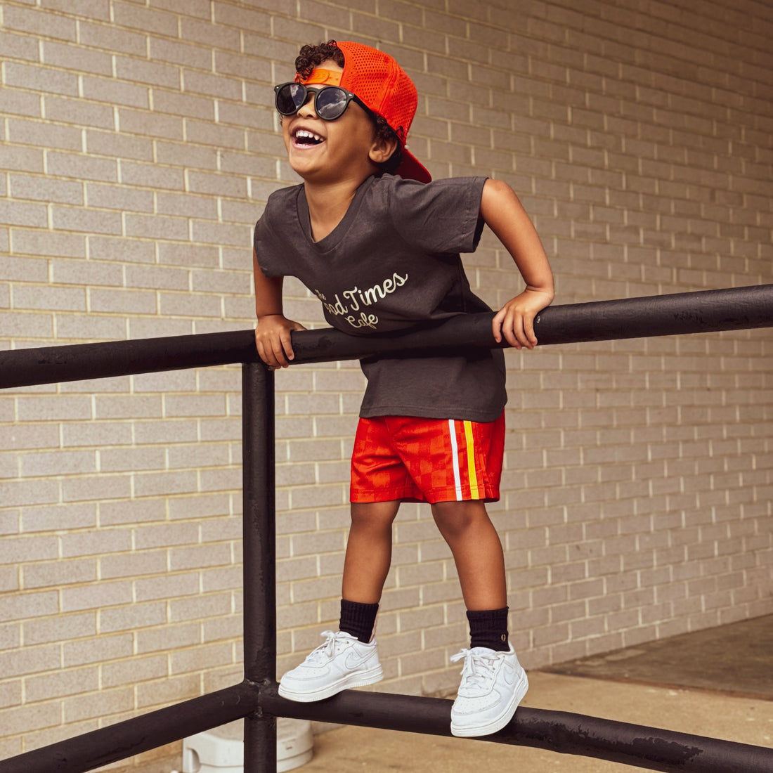 Boy wearing red/orange Retro-Wave hybrid board shorts with a hat and sunglasses.