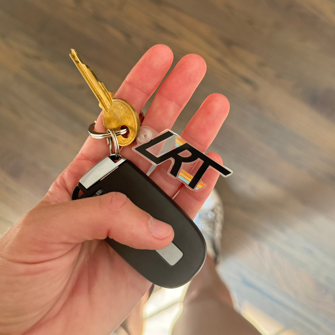 Hand holding a clear LRT logo keychain with keys and a car remote.