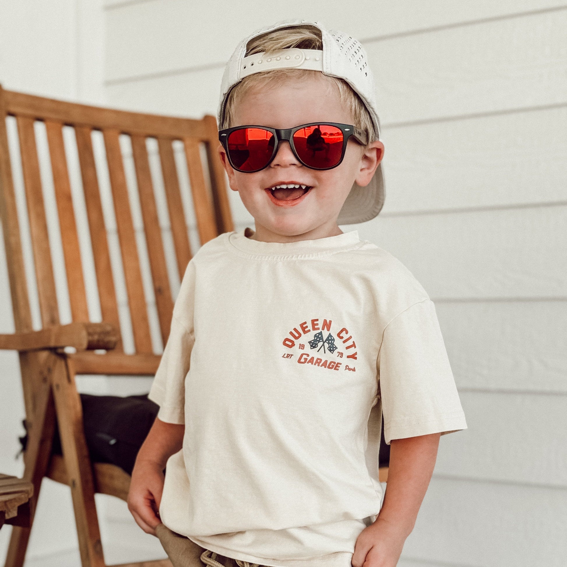 Young boy wearing the Queen City Garage Tee in vintage cream with red sunglasses.