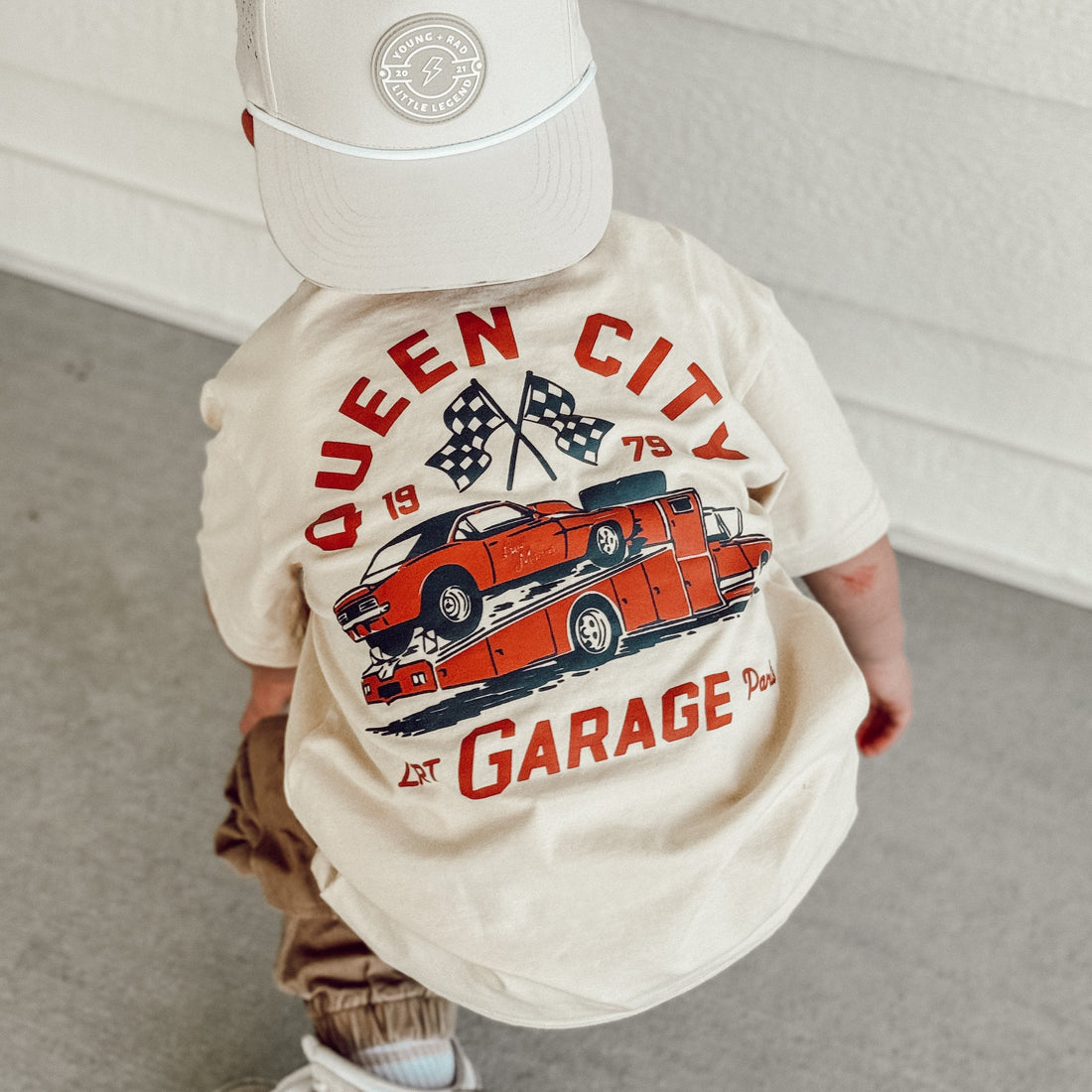 Toddler wearing Queen City Garage Tee with a retro racing graphic on a cream shirt.