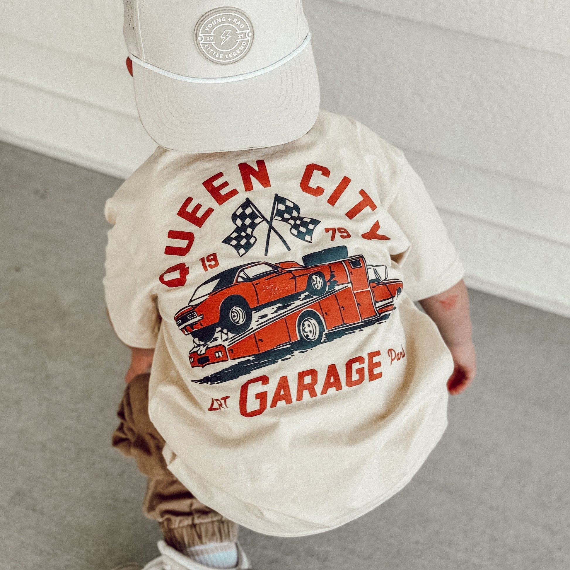 Toddler wearing Queen City Garage Tee with a retro racing graphic on a cream shirt.