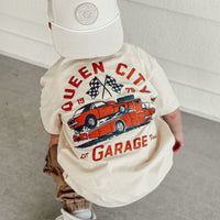 Toddler wearing Queen City Garage Tee with a retro racing graphic on a cream shirt.