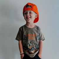 Smiling boy wearing Grand Prix military green tee with orange cap.