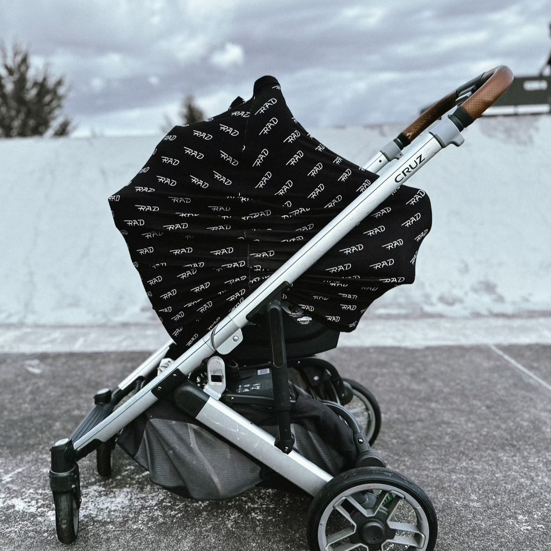 Black 'RAD' print car seat cover on a silver stroller.
