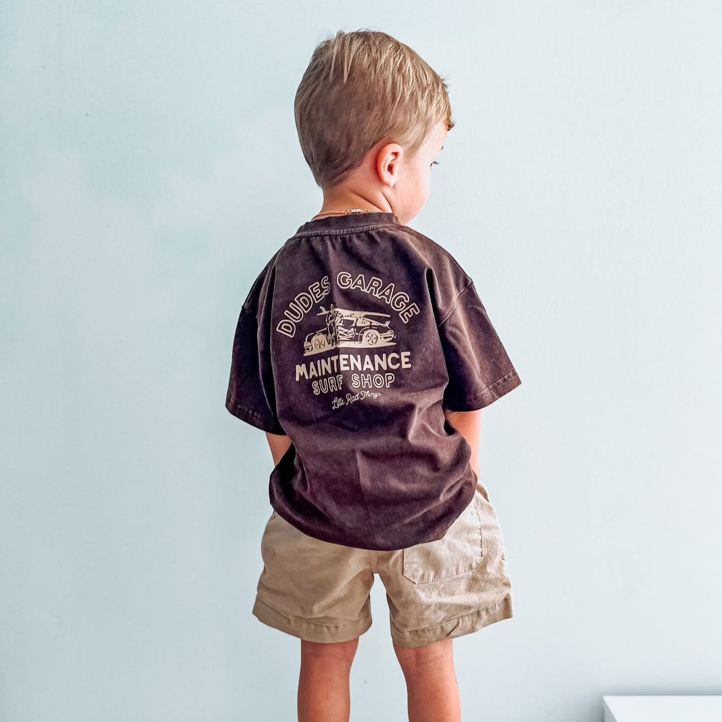 Dudes Garage vintage brown tee featuring surf shop graphic on boy outdoors.