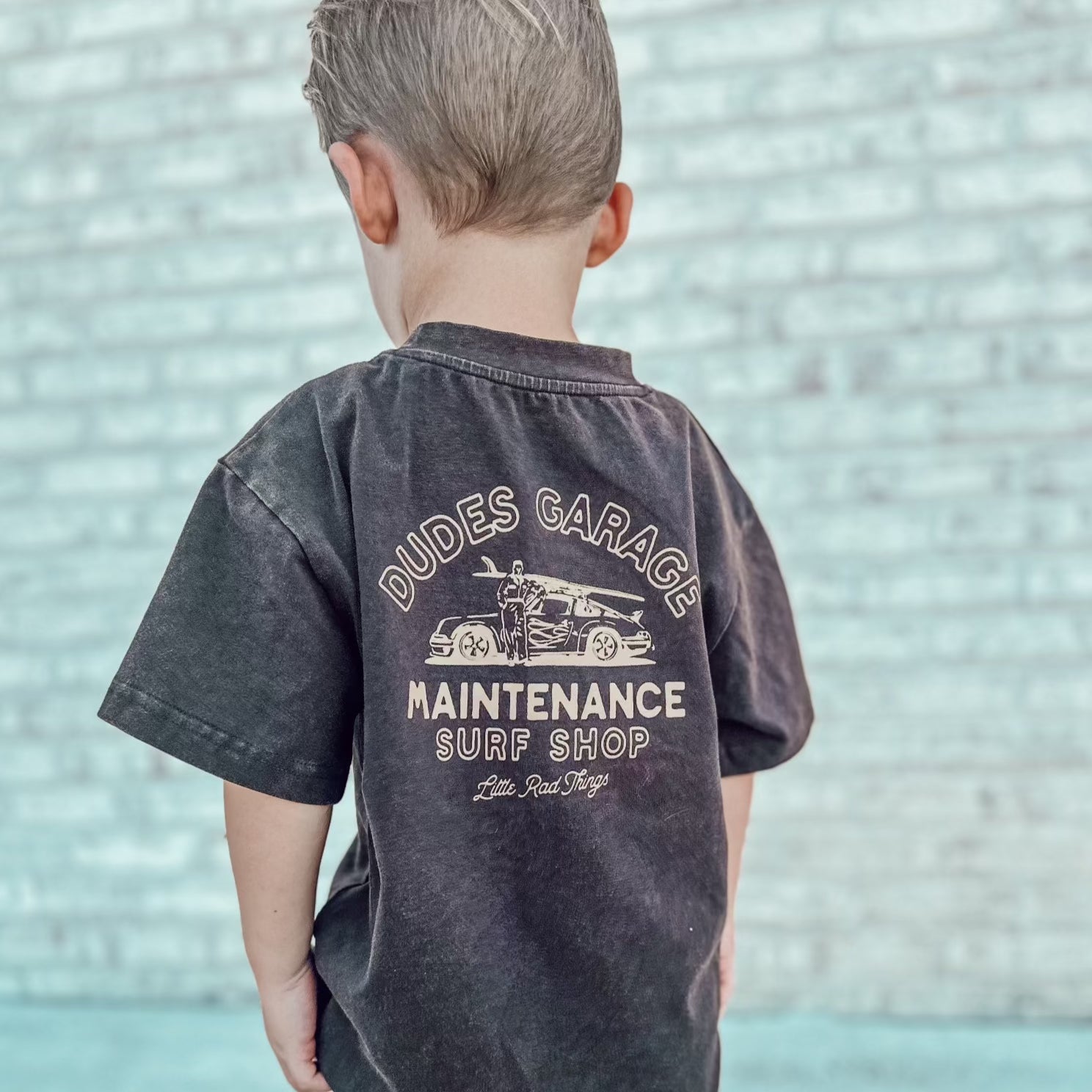 Dudes Garage vintage brown tee featuring surf shop graphic on boy outdoors.