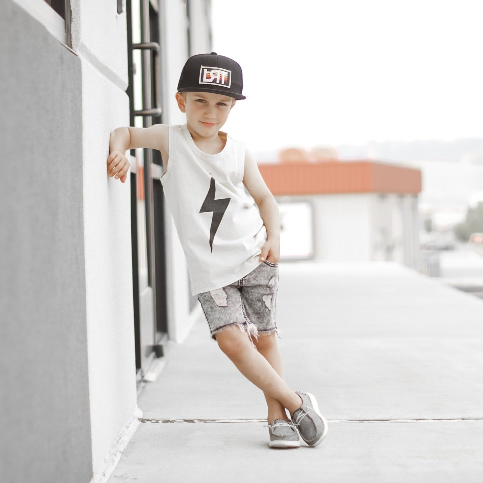 Toddler boy with lollipop wears greige Spark Muscle Tank