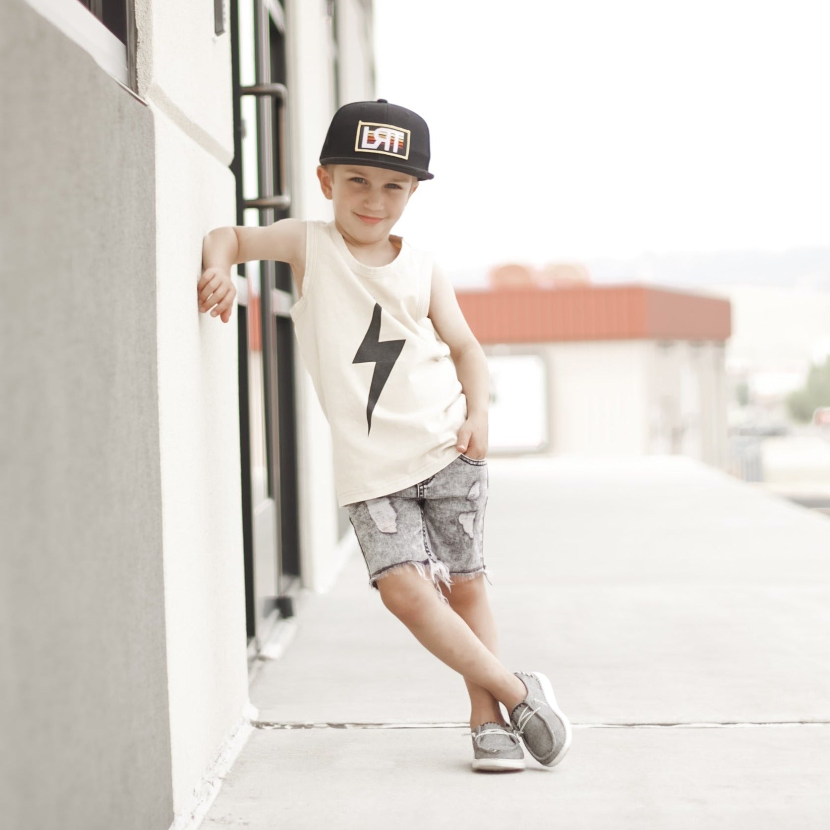 Toddler boy with lollipop wears greige Spark Muscle Tank