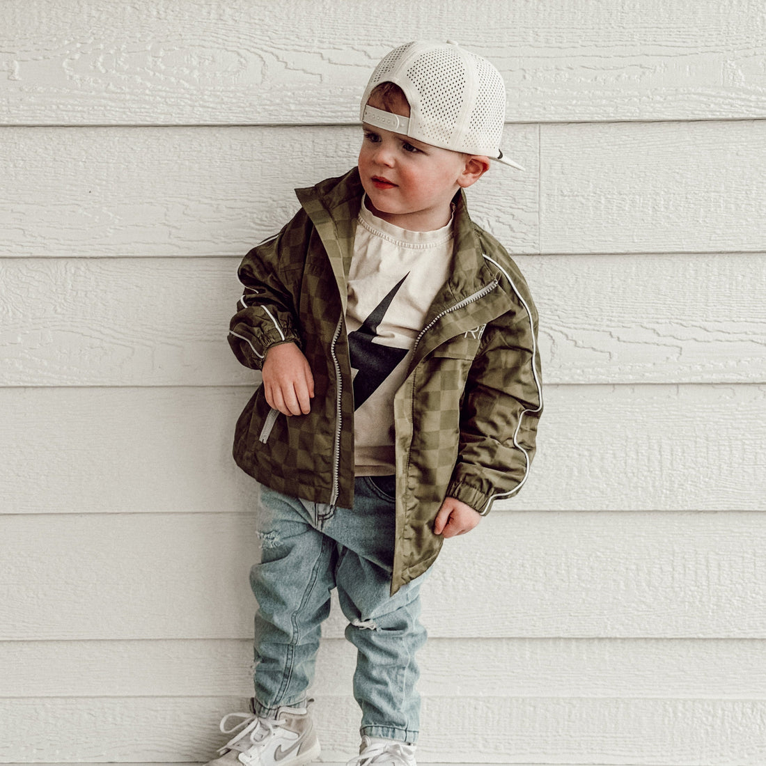 Toddler wearing the army green Storm Rider waterproof jacket with checkerboard pattern.