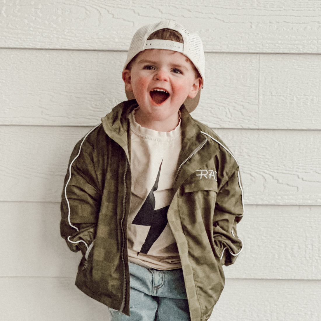 Boy wearing the Storm Rider waterproof jacket in army green, with a checkerboard pattern and white accents.
