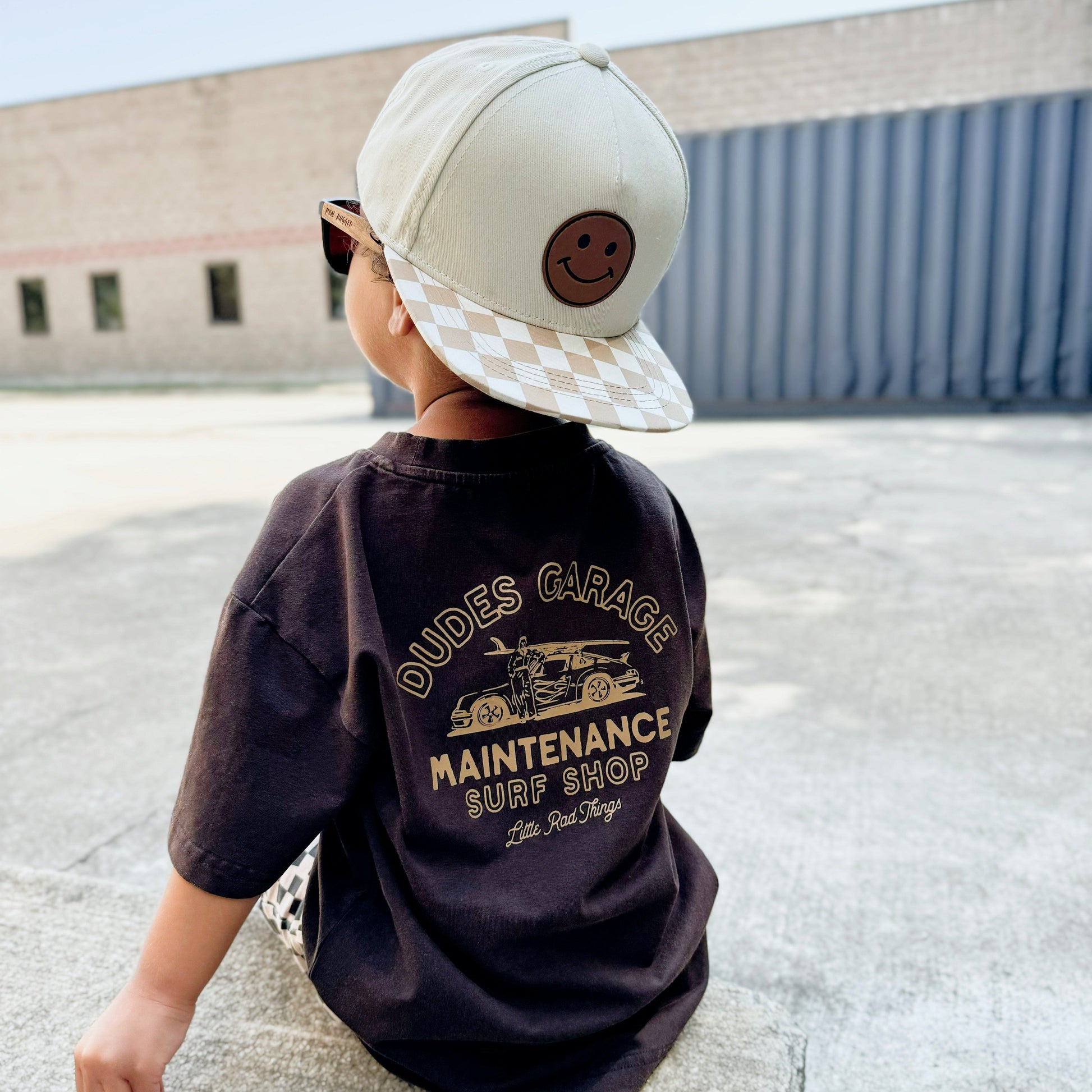 Dudes Garage vintage brown tee featuring surf shop graphic on boy outdoors.