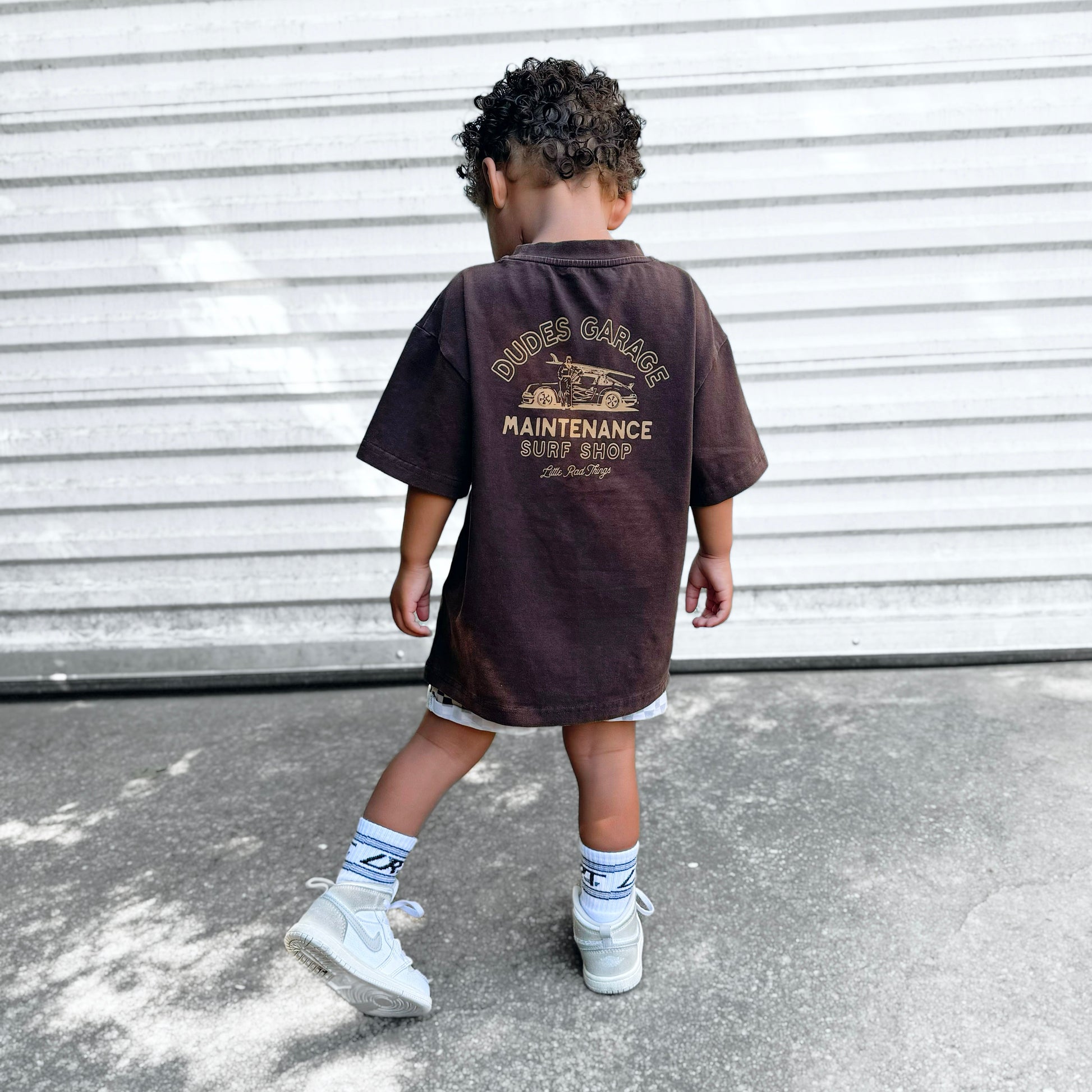 Dudes Garage vintage brown tee featuring surf shop graphic on boy outdoors.