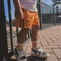 Child wearing yellow checkerboard board shorts and sneakers.