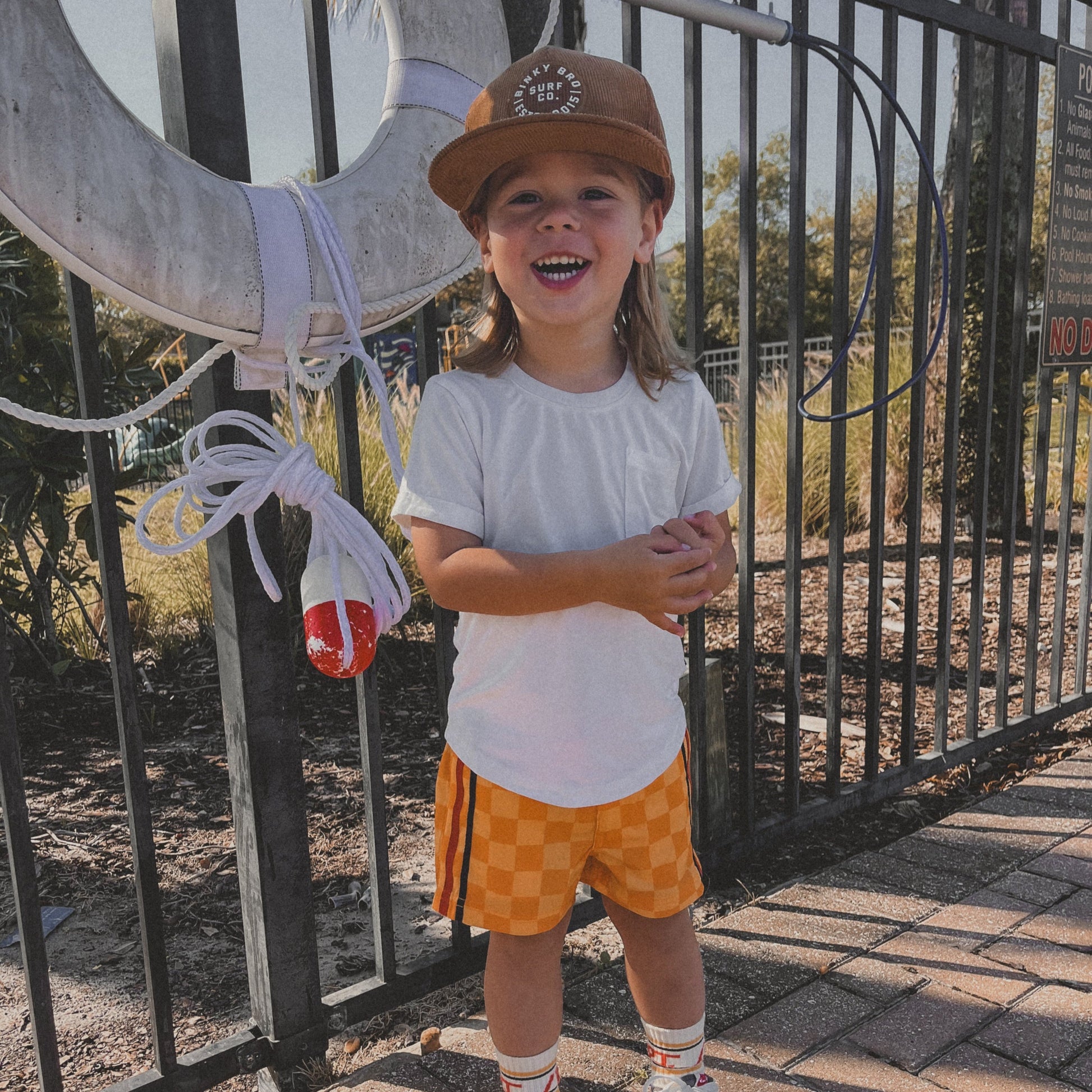 Happy kid in retro-wave yellow board shorts, hat, and t-shirt.