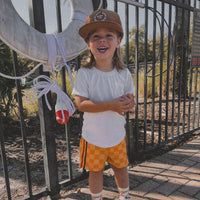 Happy kid in retro-wave yellow board shorts, hat, and t-shirt.