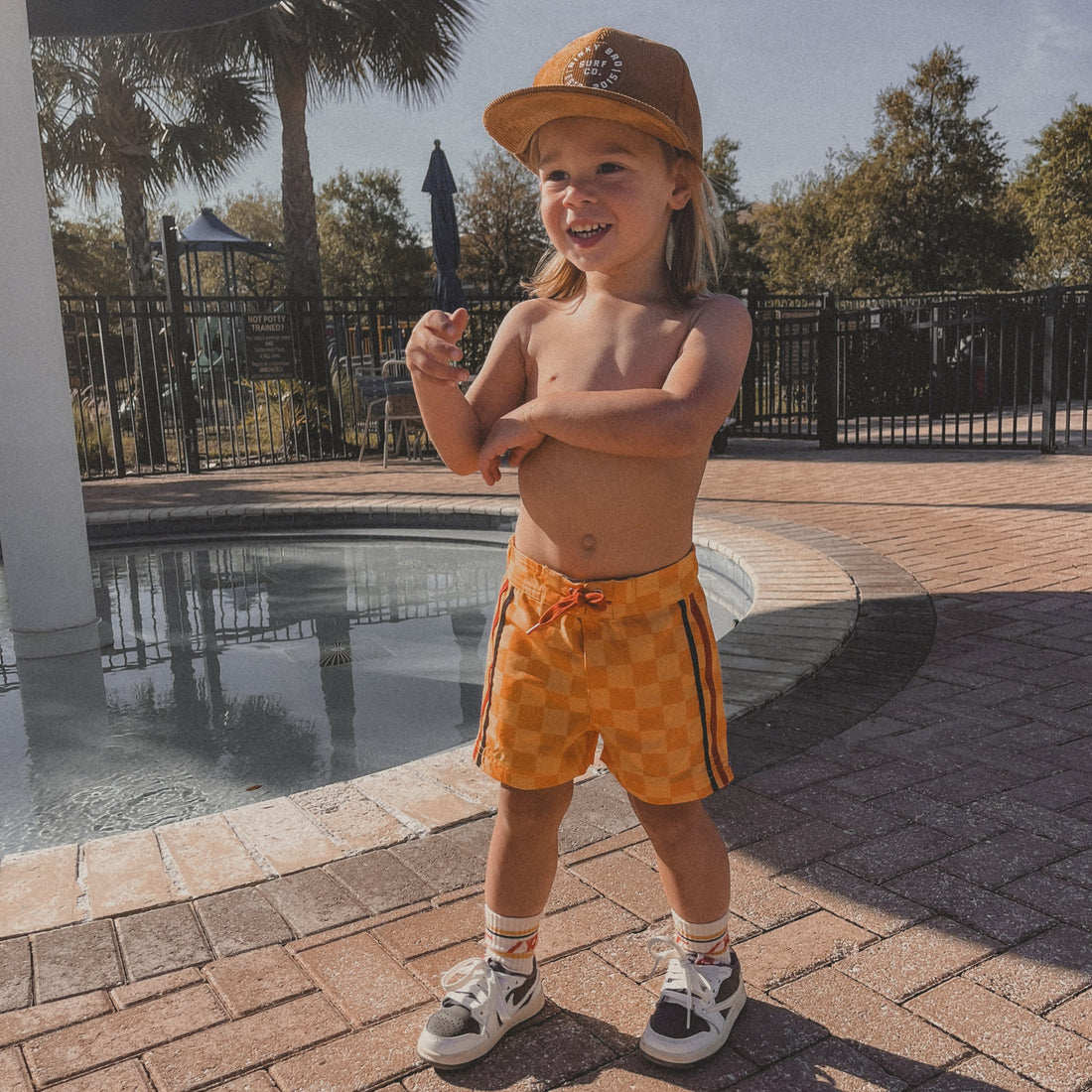 Toddler wearing retro-wave checkerboard swim trunks near the pool.