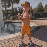 Toddler wearing retro-wave checkerboard swim trunks near the pool.