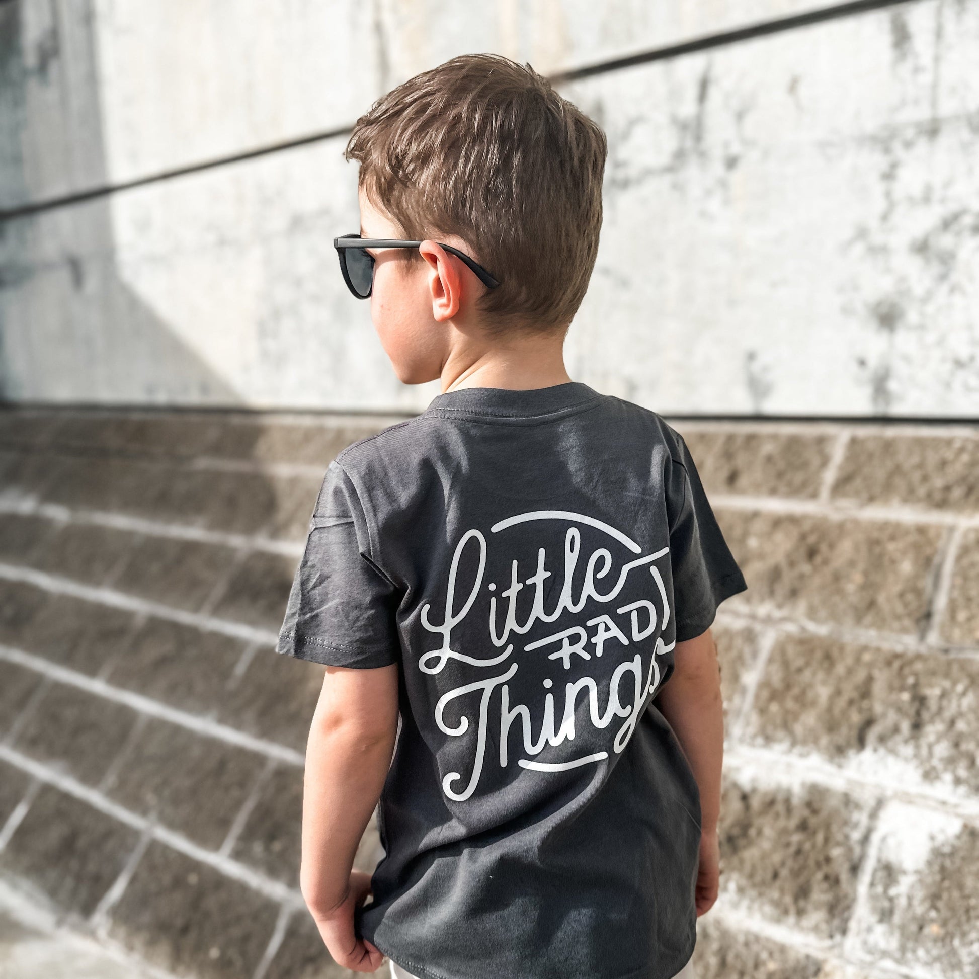 Boy in smoke RAD CIRCLE LOGO TEE with 'Little Rad Things' design, back view.