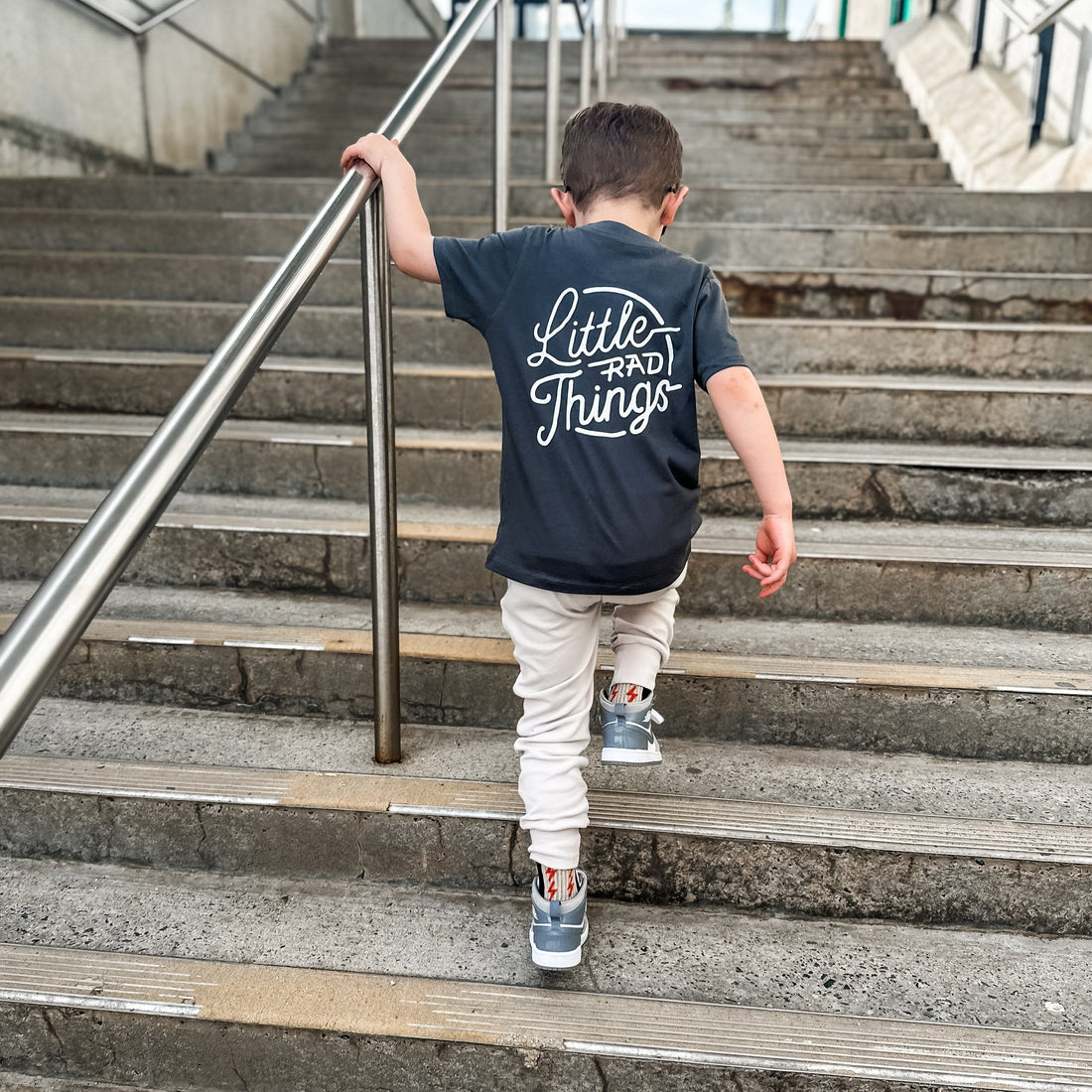Boy wearing smoke RAD CIRCLE LOGO TEE climbing stairs.