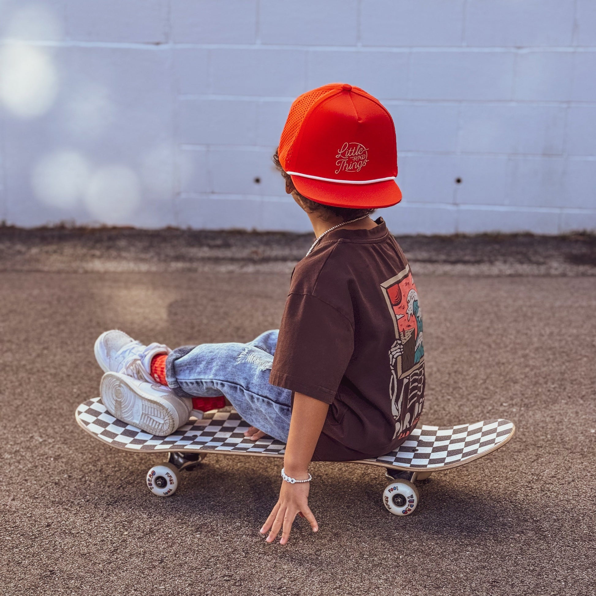 Child wearing the orange snapback hat while riding a skateboard.