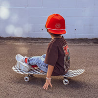 Child wearing the orange snapback hat while riding a skateboard.
