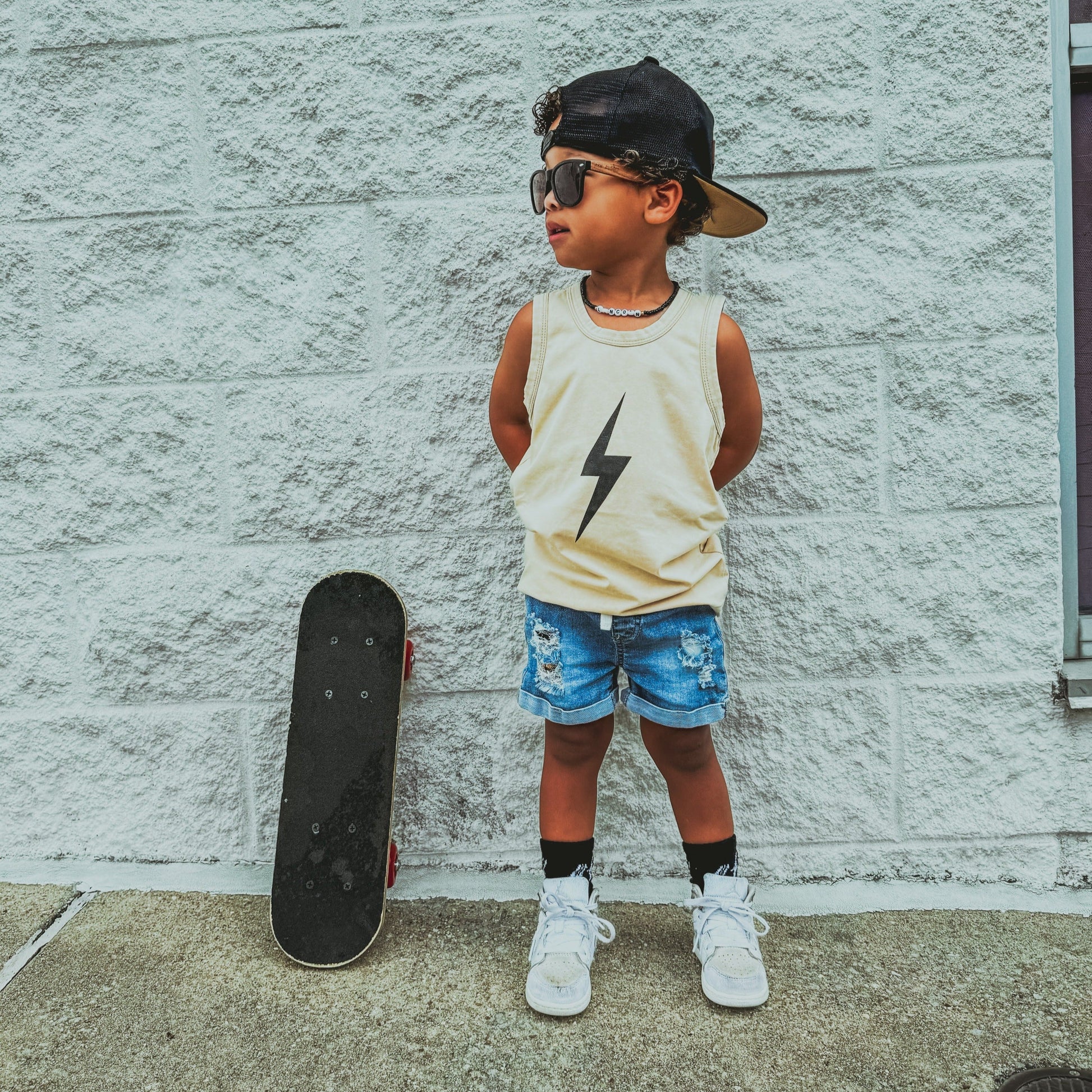 Toddler boy with lollipop wears greige Spark Muscle Tank