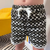 Child wearing black, grey, and white checkered 'Check Ya Later' shorts with pockets.