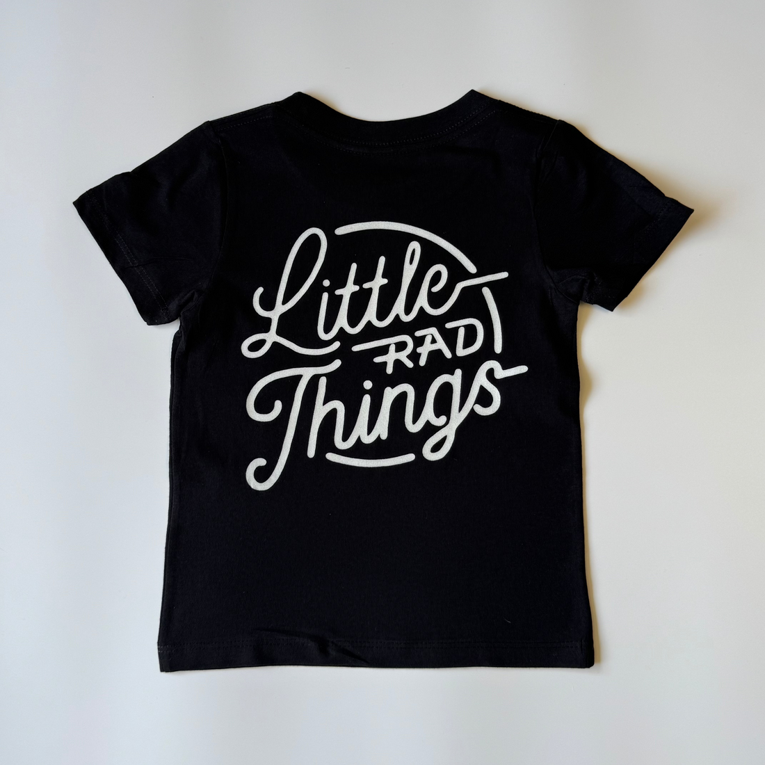 RAD CIRCLE LOGO TEE in black with 'Little Rad Things' design, laid flat.