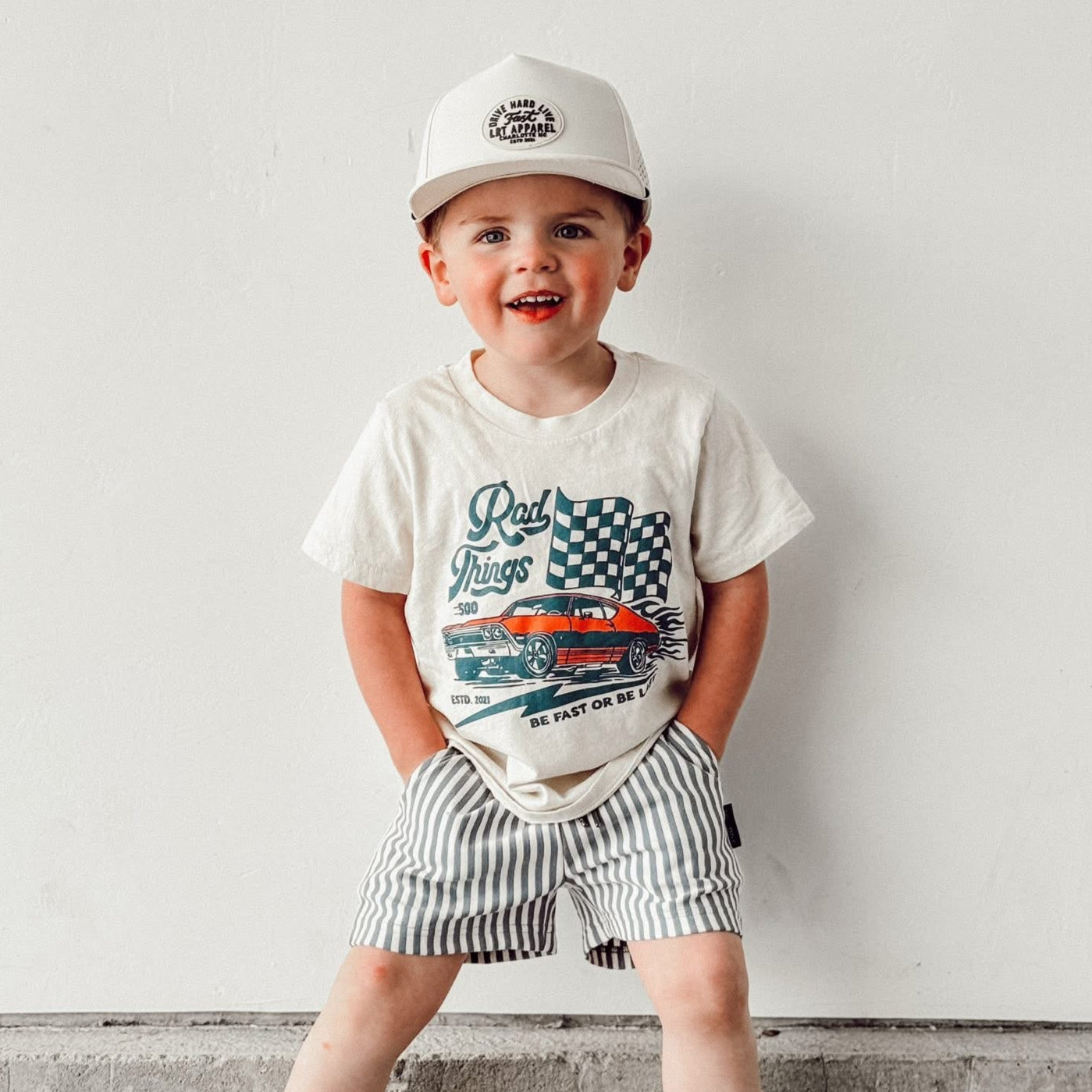 Toddler wearing Rad Things 500 tee with hat and striped shorts.