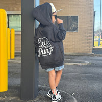Smiling child in grey Radiator Hoodie, leaning against yellow poles.