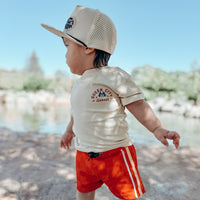 Boy wearing red/orange Retro-Wave hybrid board shorts running on the beach.