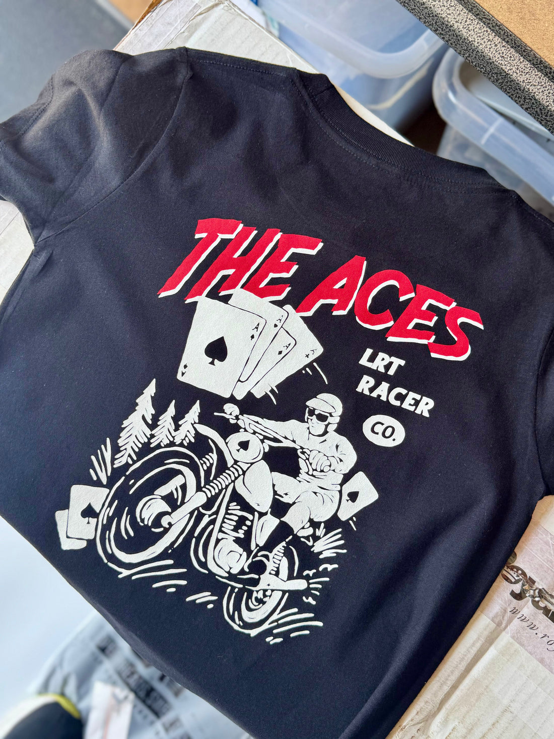 The Aces Tee: Close-up of black tee with 'The Aces' and racer graphic.