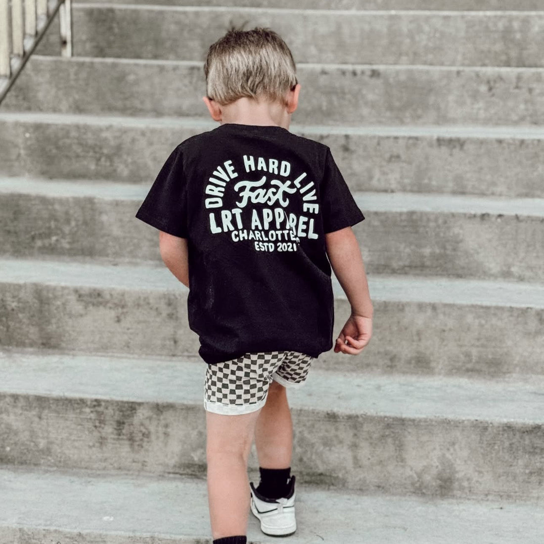 Child wearing black APEX LIVE FAST tee climbing concrete stairs.