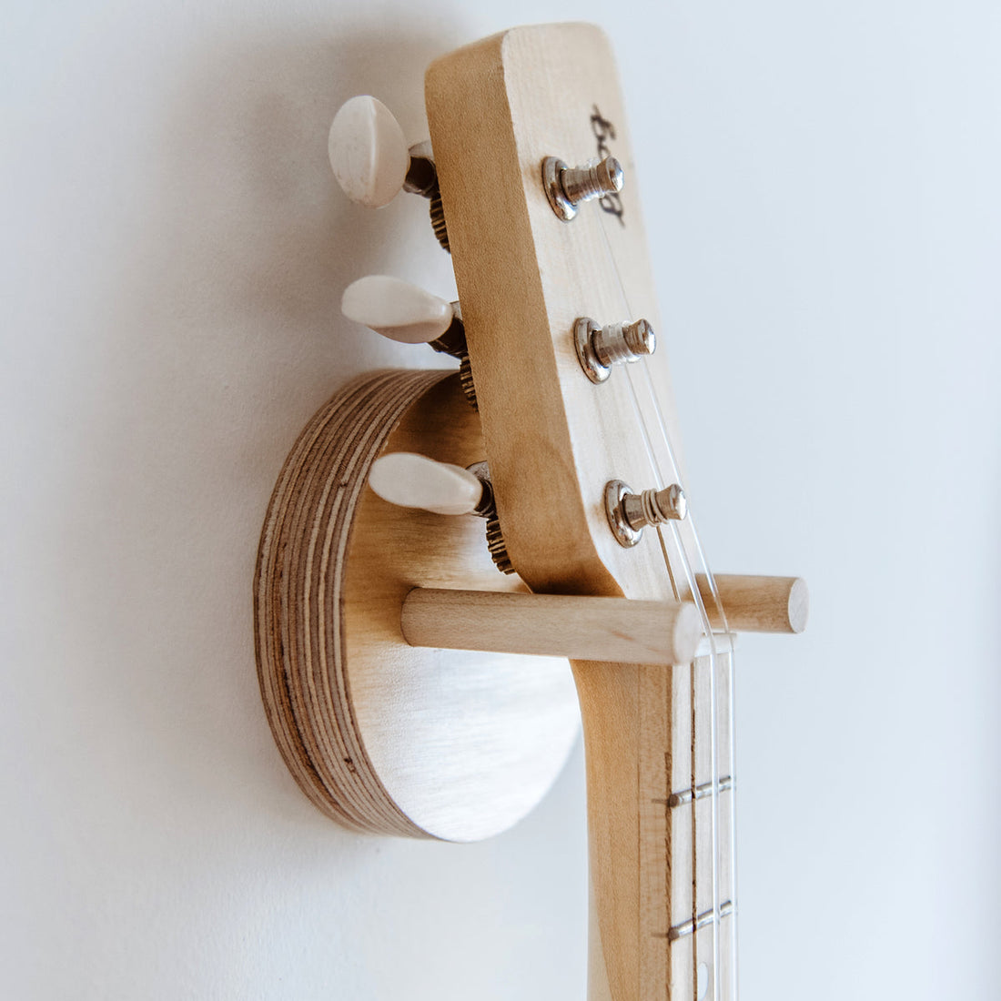 Close-up of a Loog guitar headstock mounted on a birch wall hanger.